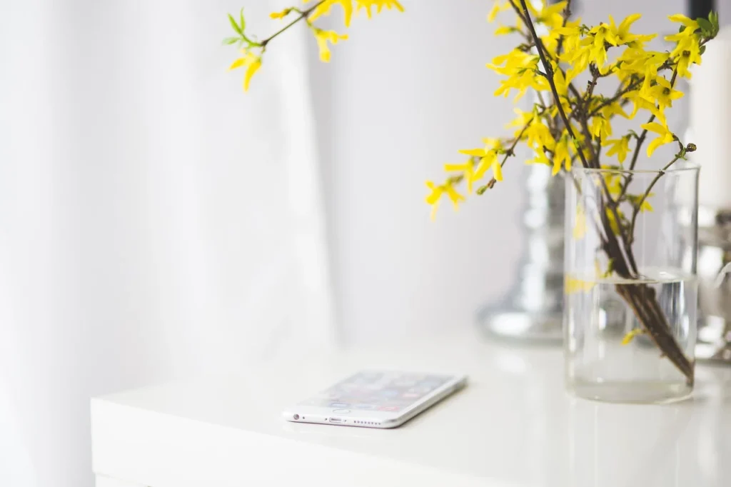 Goldregen in Vase steht auf einem weißen Tisch, daneben ein Smartphone